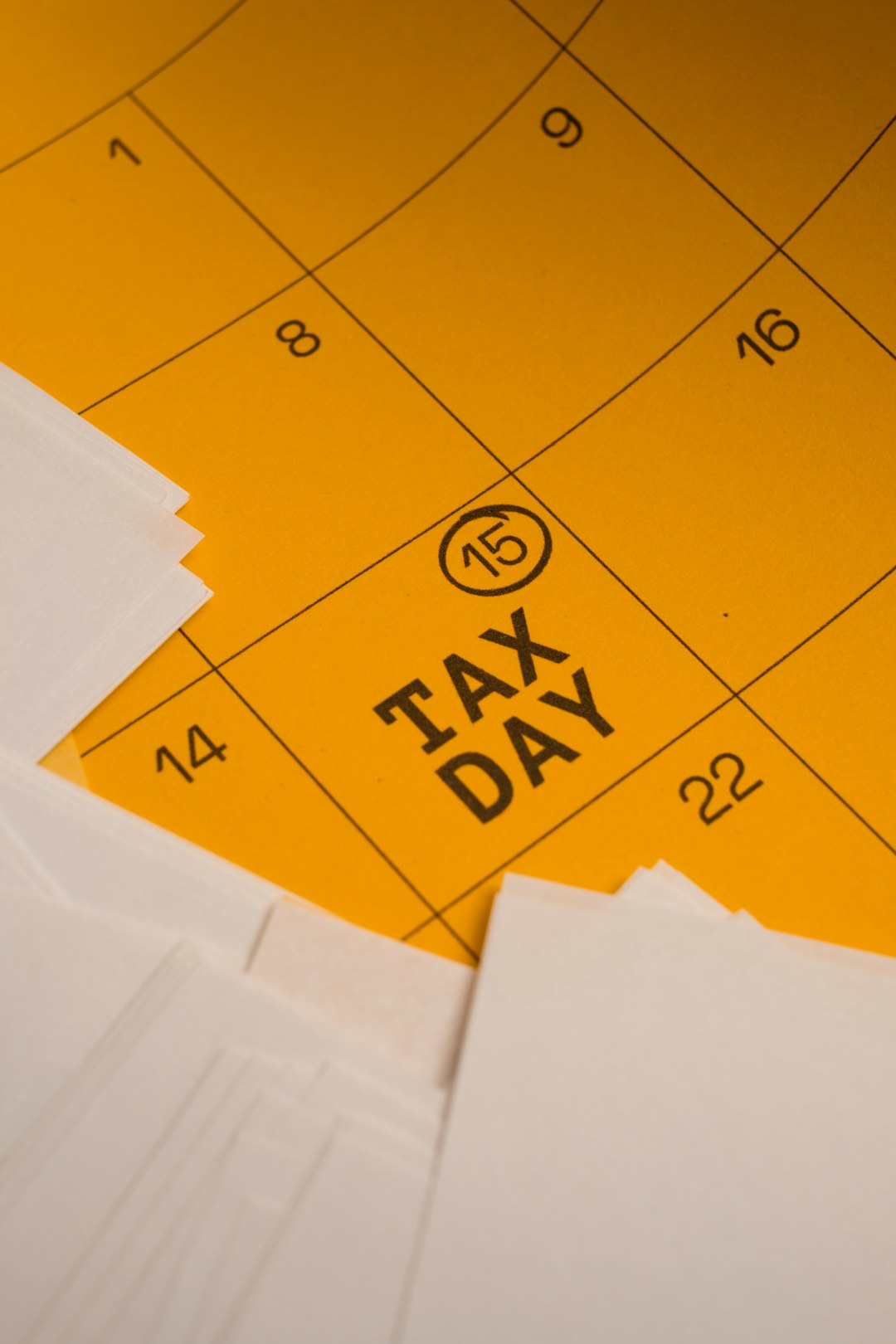 Tax Day. Yellow Wall Calendar Marked Tax Day April 15 and Surrounded by Stacks of Paperwork. Top View